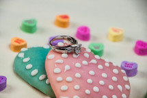 A diamond engagement ring laying on Valentine cookies and candies.