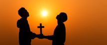 silhouettes of two people holding a cross and praying at sunset 
