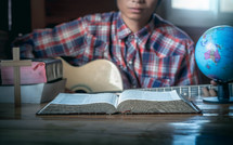 a young man playing a guitar in front of an open Bible 