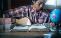 a young man playing a guitar in front of a Bible 