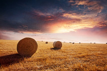 hay bales in a plowed field at sunset