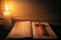 candle light with holy bible and cross on wooden table in the night time.