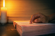 candle light with hands reading bible on wooden table in the night time.