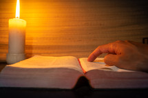 candle light with hands reading bible on wooden table in the night time.