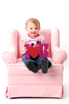 toddler sitting on a pink recliner holding an I heart you sign 