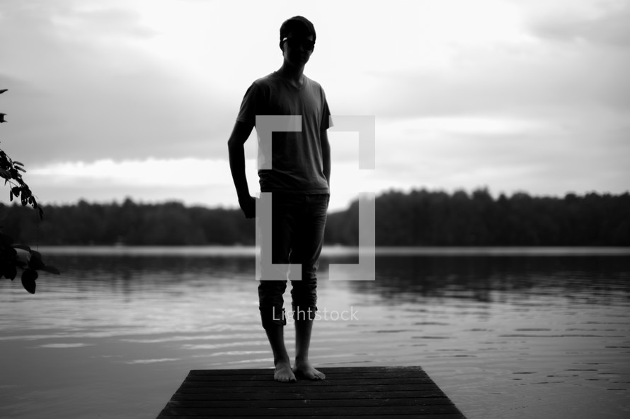 Silhouette of a man standing on a pier on a lake.