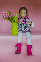 A girl child sitting with a vase of tulips 