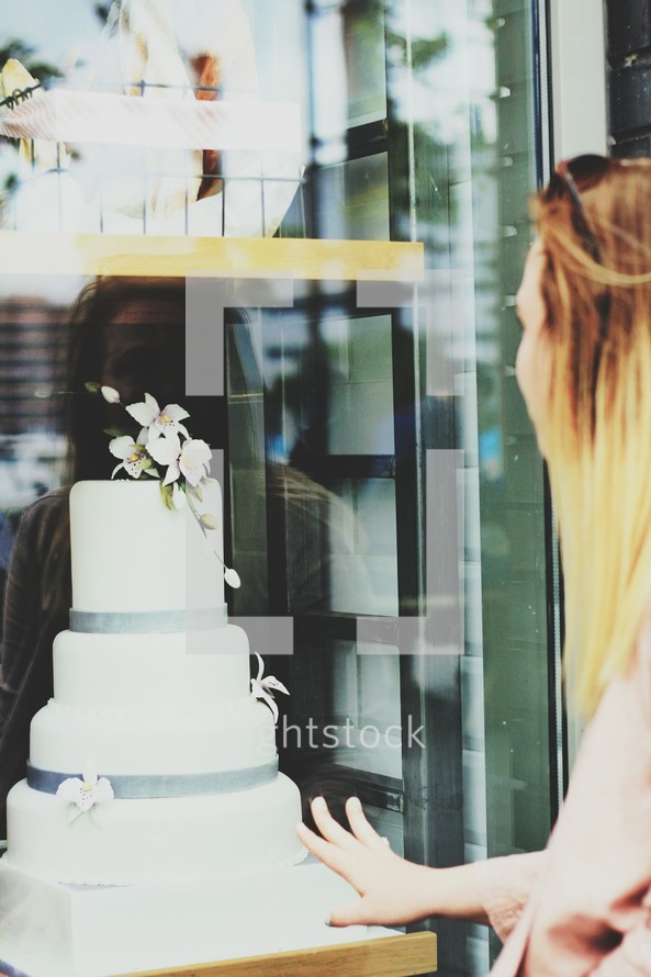 a woman looking at a wedding cake in a bakery window 