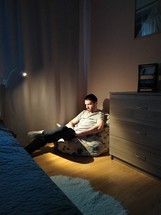 a man sitting in a dark room reading a Bible in a corner 