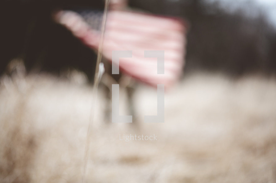 out of focus soldier in a field holding an American flag 