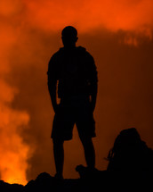 a silhouette of a man standing in front of a forest fire 