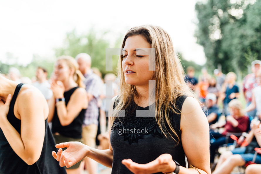 a woman at an outdoor worship service with hands raised 