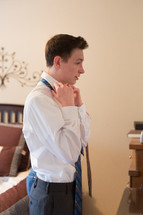 a teenage boy putting on a necktie 