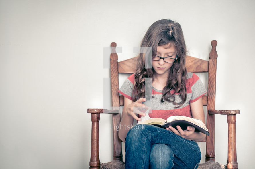 girl child sitting in a chair reading a Bible 