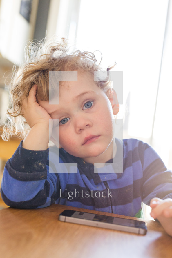 an exhausted toddler boy next to a cellphone 
