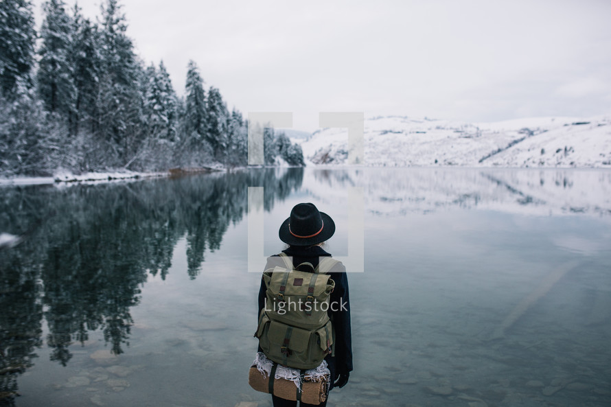 a woman backpacking near a snowy lake shore 