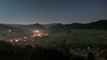 Calm starry night sky with stars over countryside nature with busy traffic in small rural city time-lapse
