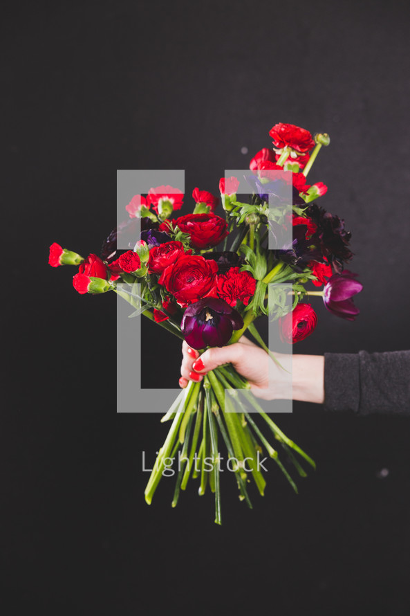 hand holding out a bouquet of red and purple flowers 