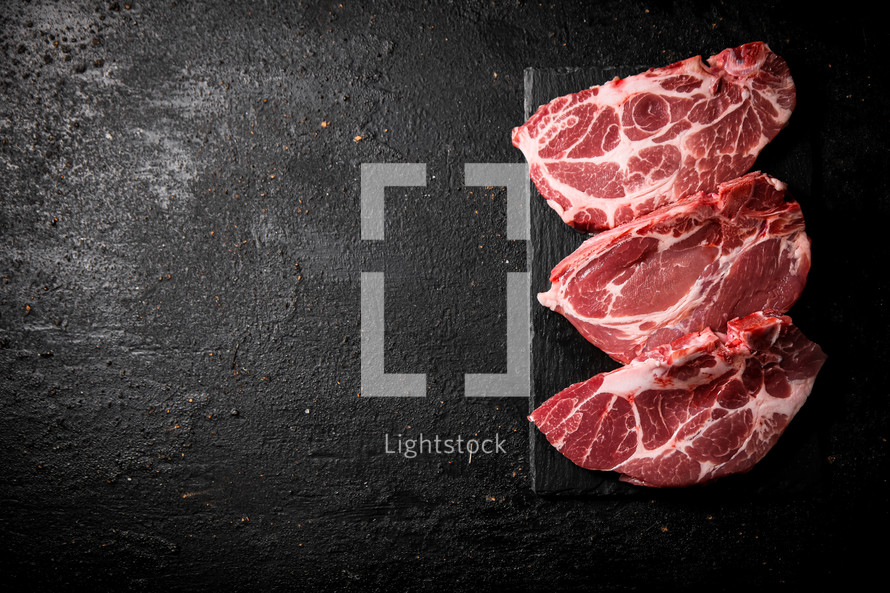 Raw pork steak on a stone board. On a black background. High quality photo