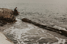 a man sitting on a rocky shore 