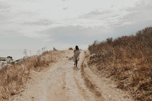 a woman walking on a dirt road along a shore 