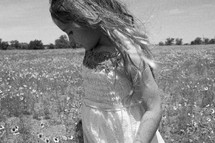 a girl child in a sundress walking through a field of wildflowers 