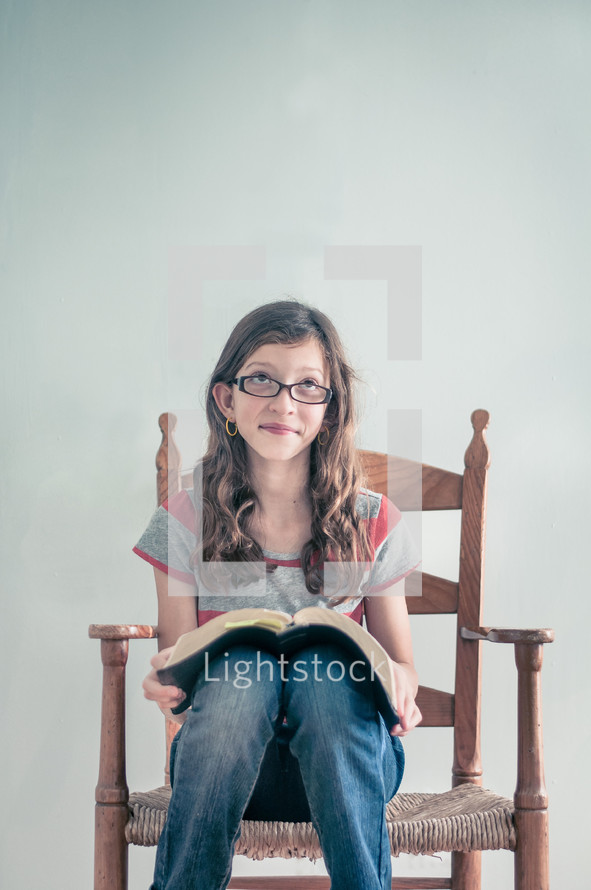 Girl sitting in a chair reading her bible - with a facial impression of thinking something nice.