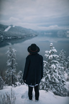 a woman standing at the edge of a snowy cliff looking down at water below 