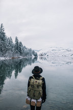 a woman with a backpack standing in front of a winter lake 