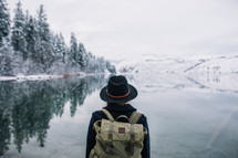 a woman with a backpack standing by a snowy lake shore 