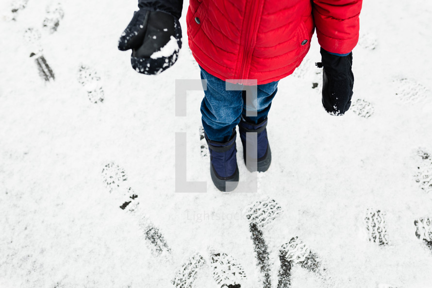 child in snow boots standing in snow 