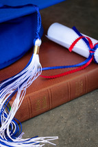 diploma, Bible, and blue graduation cap with tassel 