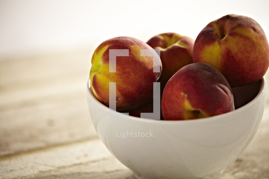 A bowl of peaches sit on a wooden table.
