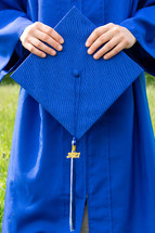 female graduate outdoors holding a graduation cap 