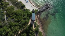 Cinematic Aerial  pull-back view of the lighthouse, tourist and the beach