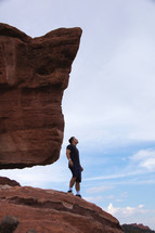 man standing on red rock looking upward