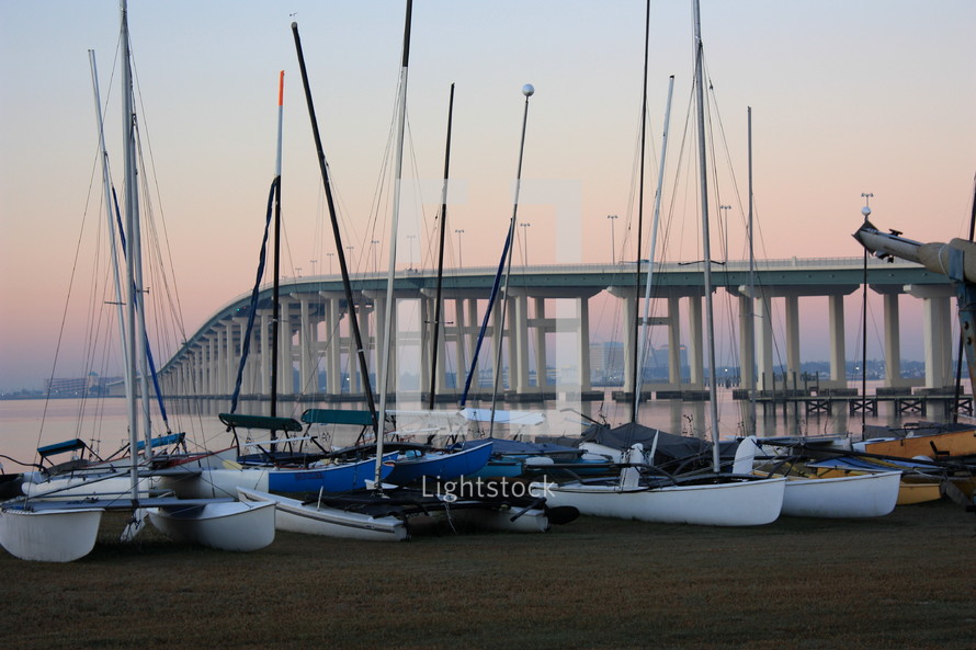 multiple sailboats,  moored,  with a bridge in the background