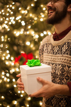a man holding a gift in front of a Christmas tree at a Christmas party 