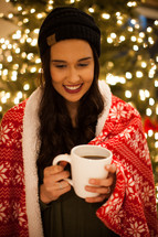 a woman wrapped in a blanket holding a mug of hot cocoa 
