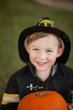 a boy in a fire fighter costume holding a pumpkin 