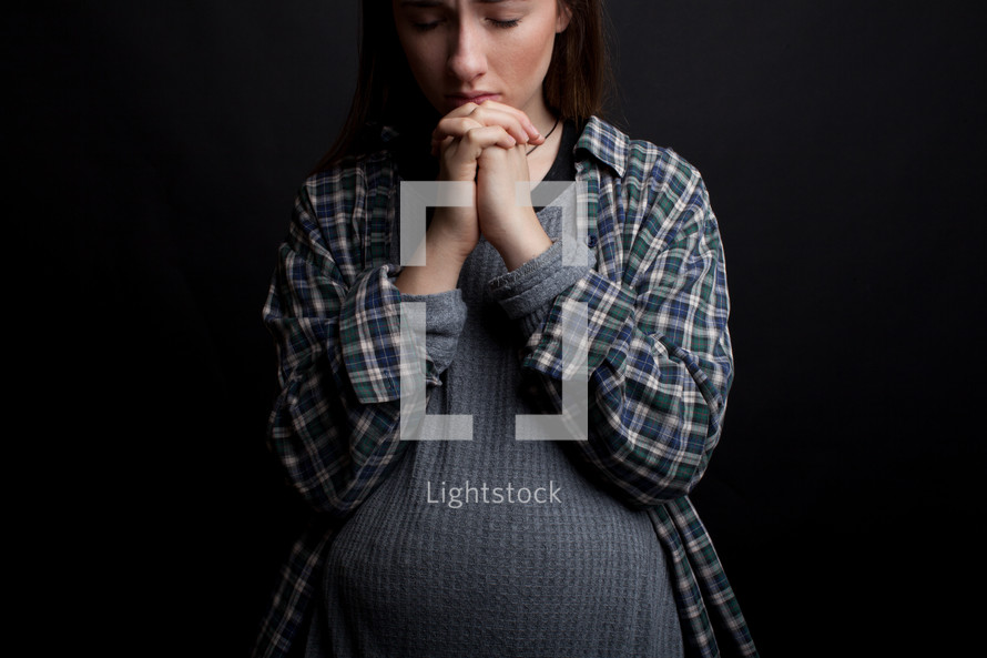 teen girl with a pregnant belly praying 