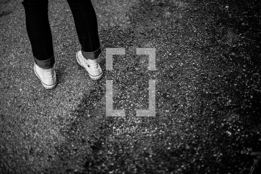 A teen girl's feet standing on asphalt.