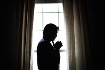 silhouette of an Indian man in prayer in front of a window 