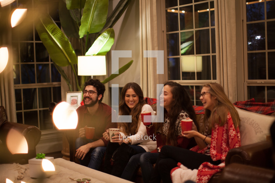 people sitting on a couch drinking hot cocoa and talking at a Christmas party 