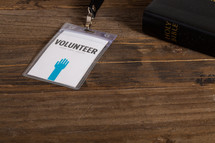 A volunteer badge holder on a table next to a Bible.
