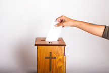 A hand putting an offering into an offering box.
