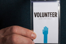 A hand holding a volunteer badge.