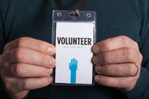 A man holding a volunteer badge with both hands.