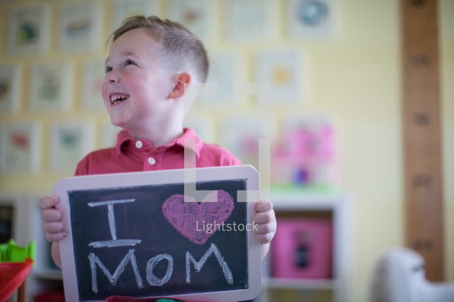 a little boy holding a chalkboard sign that reads I heart mom 