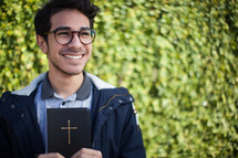 smiling man holding a Bible outdoors 
